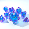 A collection of handmade resin D20 dice in blue and purple liquid swirl, scattered on a white surface.