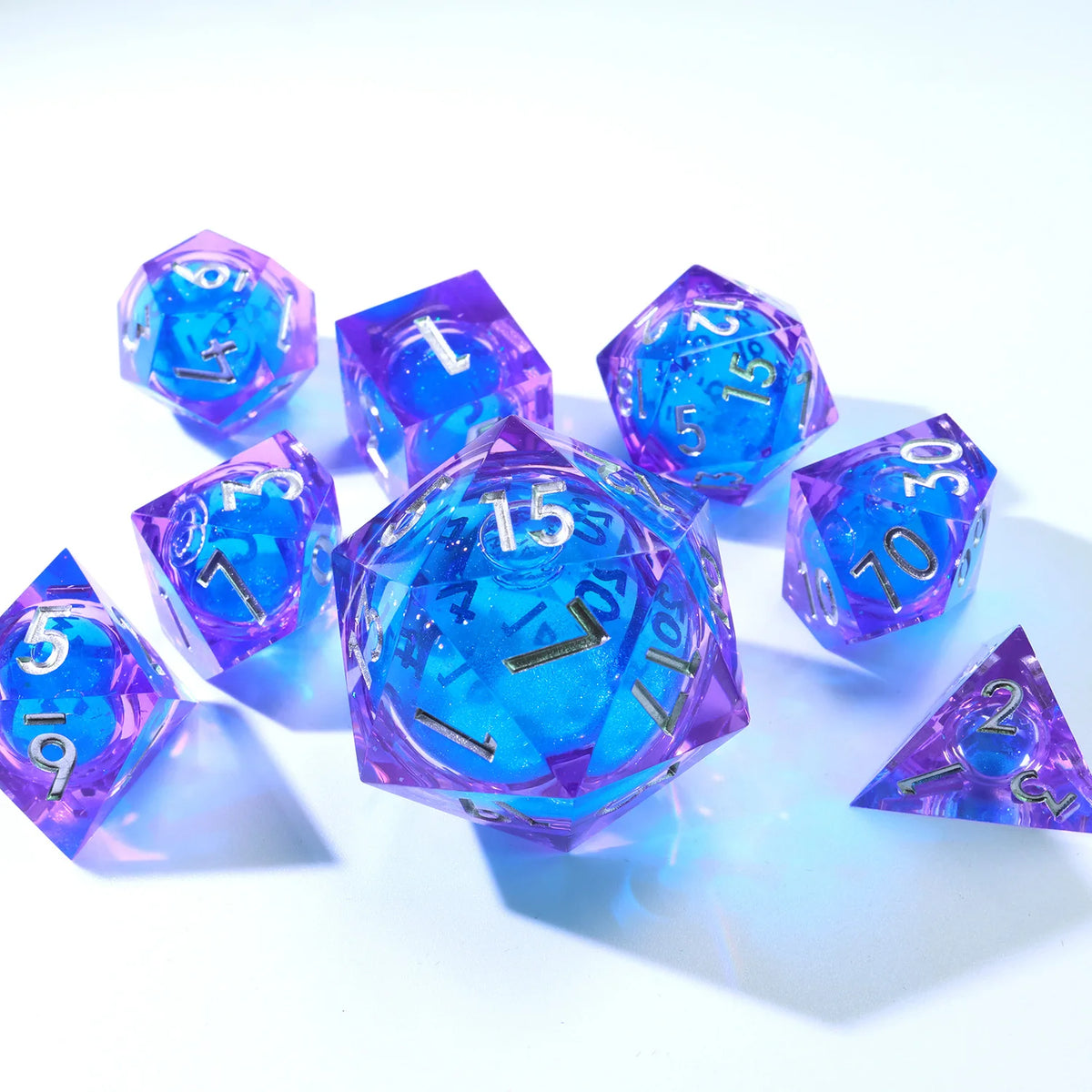 A collection of handmade resin D20 dice in blue and purple liquid swirl, scattered on a white surface.