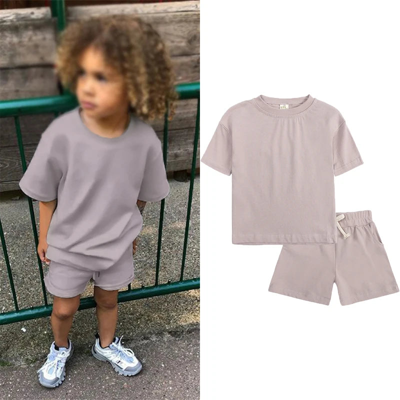 A young child wearing a light mauve short sleeve top and matching shorts outdoors.