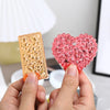 Hands hold a pink heart-shaped silicone resin mold alongside a rectangular piece of clear resin.