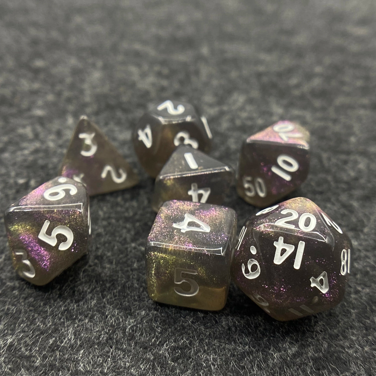 A set of seven iridescent acrylic polyhedral dice with a velvet pouch resting on a dark surface.