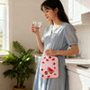 A woman holds a pink portable hot water bottle with a cozy cover in a light blue dress in a modern kitchen.