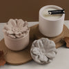A white ceramic jar with a black label sits on a cork coaster next to a pale pink silicone floral mold.