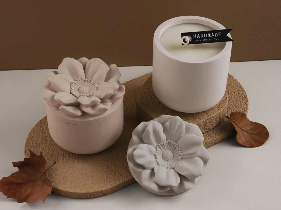 A white ceramic jar with a black label sits on a cork coaster next to a pale pink silicone floral mold.