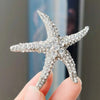 A sparkling rhinestone turtle starfish brooch pin held by a person's fingers.