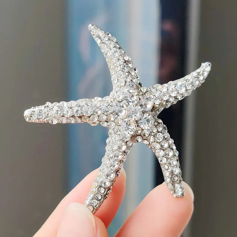A sparkling rhinestone turtle starfish brooch pin held by a person's fingers.