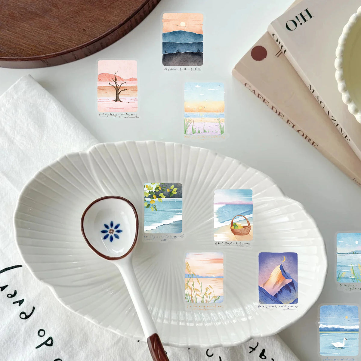 A white ceramic plate with decorative stickers featuring mountain and sea scenery is displayed on a white cloth.