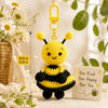 A yellow crochet bee doll with black stripes and wings hangs from a gold hook next to a motivational card.