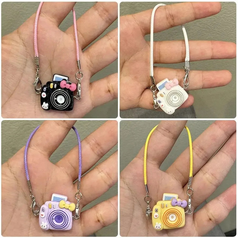 A collection of mini plush camera doll accessories in pink, white, and yellow colors displayed on a hand.