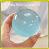 A hand holds a clear blue coconut oil squishy stress relief ball against a light background.