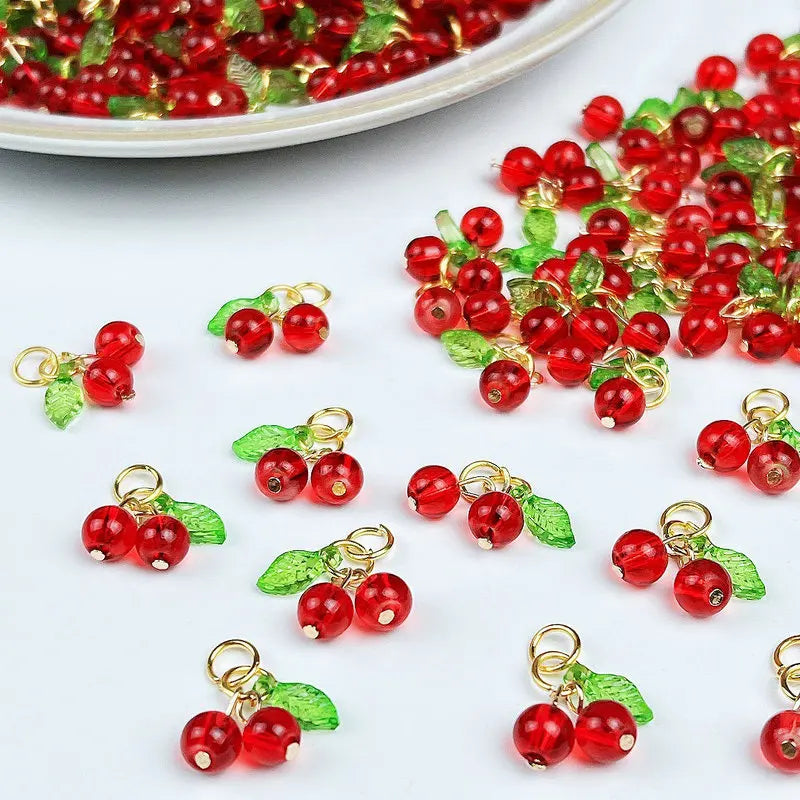 Small red cherry glass charms with gold-colored jump rings and green leaves for jewelry making