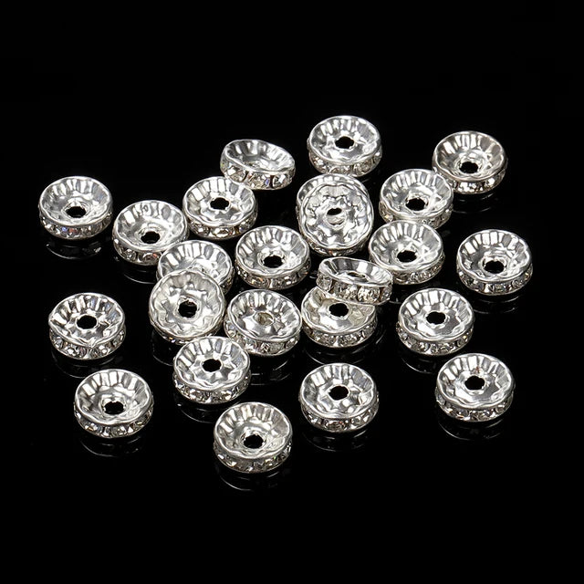 A collection of silver crystal rondelle spacer beads for jewelry making arranged on a black surface.