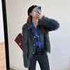 A woman wearing a dark blue shirt and black pants is posing while taking a photo with her phone, featuring a fluffy gray knit