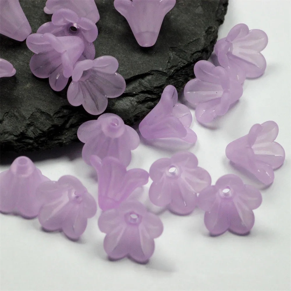 A collection of small, translucent lavender frosted acrylic flower beads scattered on a dark surface.