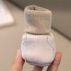A pair of beige baby soft sole first walker shoes with a knitted cuff and suede-like upper being held by a hand.