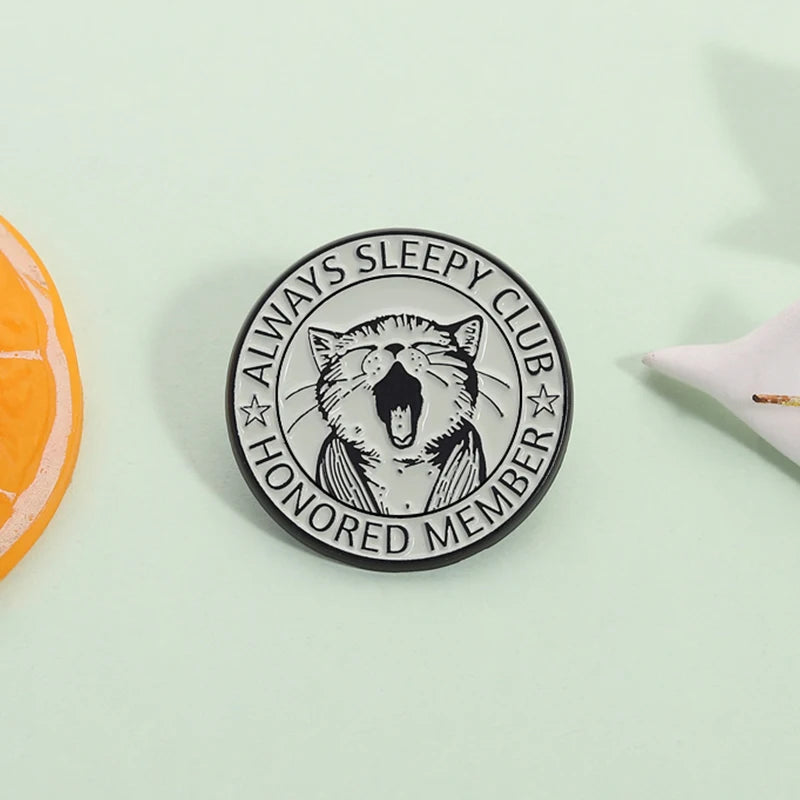 Black enamel pin featuring a detailed illustration of a cat with an open mouth and stars, labeled as a honored member of the 