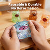 A hand holds a transparent glitter capybara slow-rising squishy toy against a wooden background.