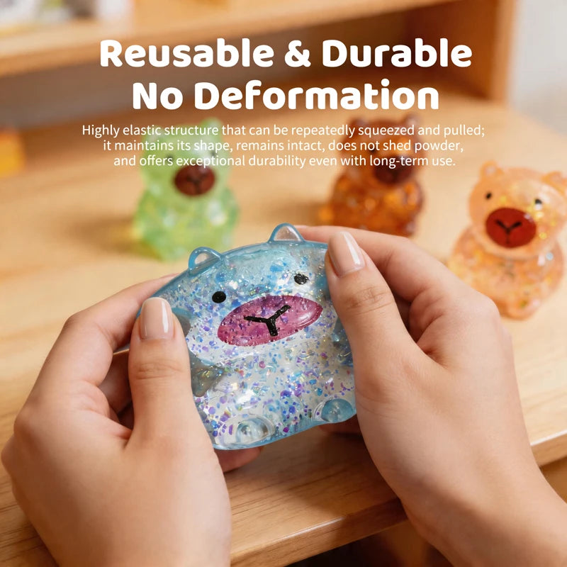 A hand holds a transparent glitter capybara slow-rising squishy toy against a wooden background.