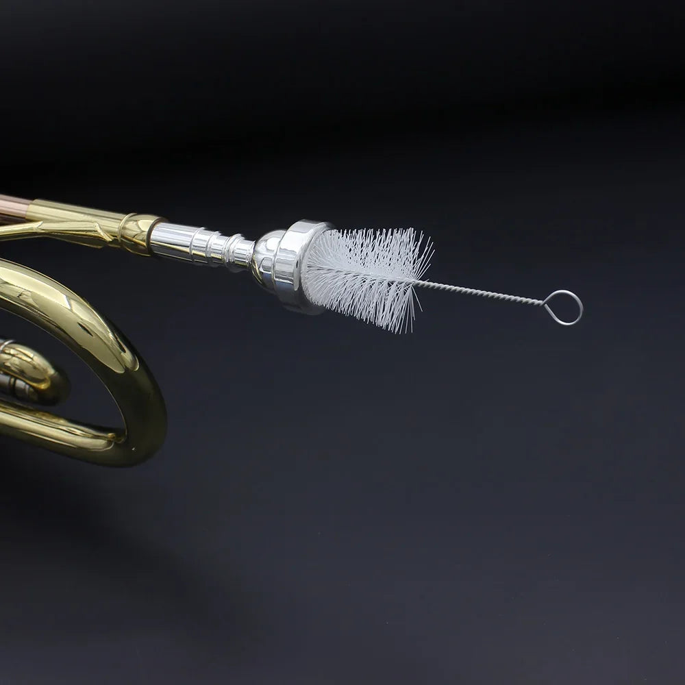 A brass trumpet cleaning kit with a piston and mouthpiece brush is shown against a dark background.