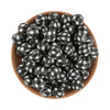 A pile of black and white plaid silicone beads for jewelry making in a wooden bowl.