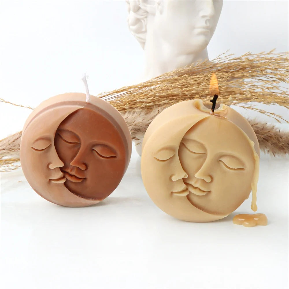 Two silicone molds shaped like serene faces for candles or soap making resting on straw