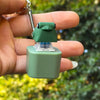 A hand holds a green LED frog croaking keychain fidget toy with a metal clip.