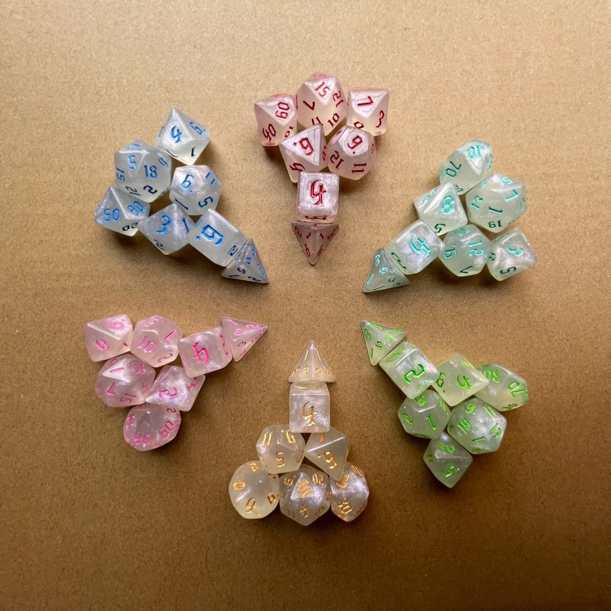 A collection of seven glitter gold polyhedral dice in various colors and sizes scattered on a brown surface.