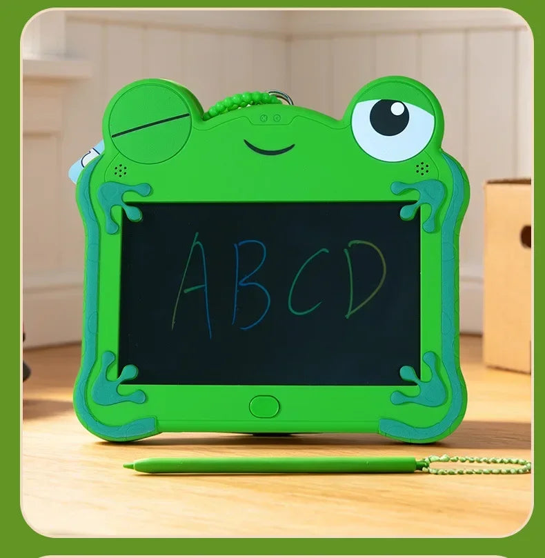 A green frog-shaped LCD drawing tablet with the letters ABCD written on the screen, resting on a wooden surface.