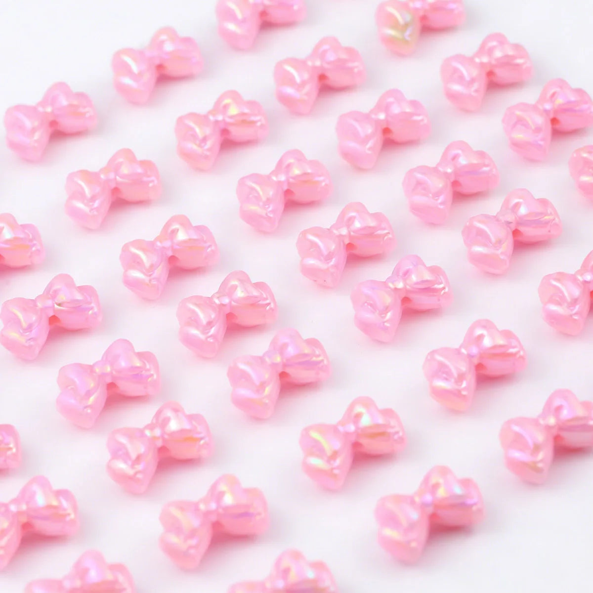 Pink acrylic bow beads scattered on a white background for jewelry making