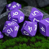 A collection of purple silicone polyhedral dice resting on green grass and dark stones.