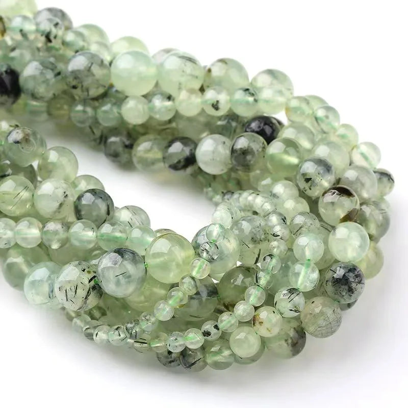 A close-up of a strand of round, translucent green and gray natural stone beads for jewelry making.