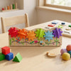 A wooden Montessori busy board for toddlers featuring colorful gears, switches, and sensory elements on a light wood table.