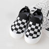 A pair of black and white checkered plaid slip-on toddler shoes for first walkers resting on a white surface.