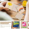 Hand holding small natural wood squares with a yellow flower design on a wooden surface
