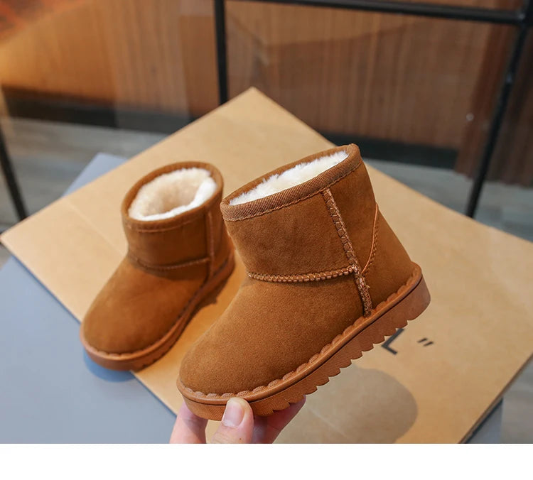 A pair of brown suede winter boots with faux fur lining are being held, resting on a cardboard box.