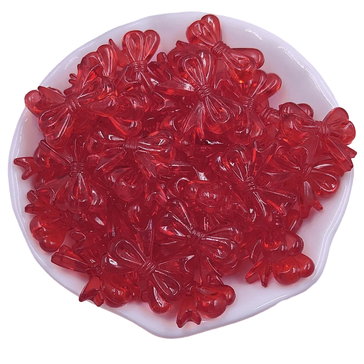 A pile of 20 red acrylic bow beads for jewelry making displayed in a white dish.