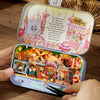 A wooden miniature dollhouse theater kit featuring a train and candy land scenery with small figures.