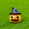 A small, orange cartoon pumpkin bear figurine with a black witch hat sitting on green grass.