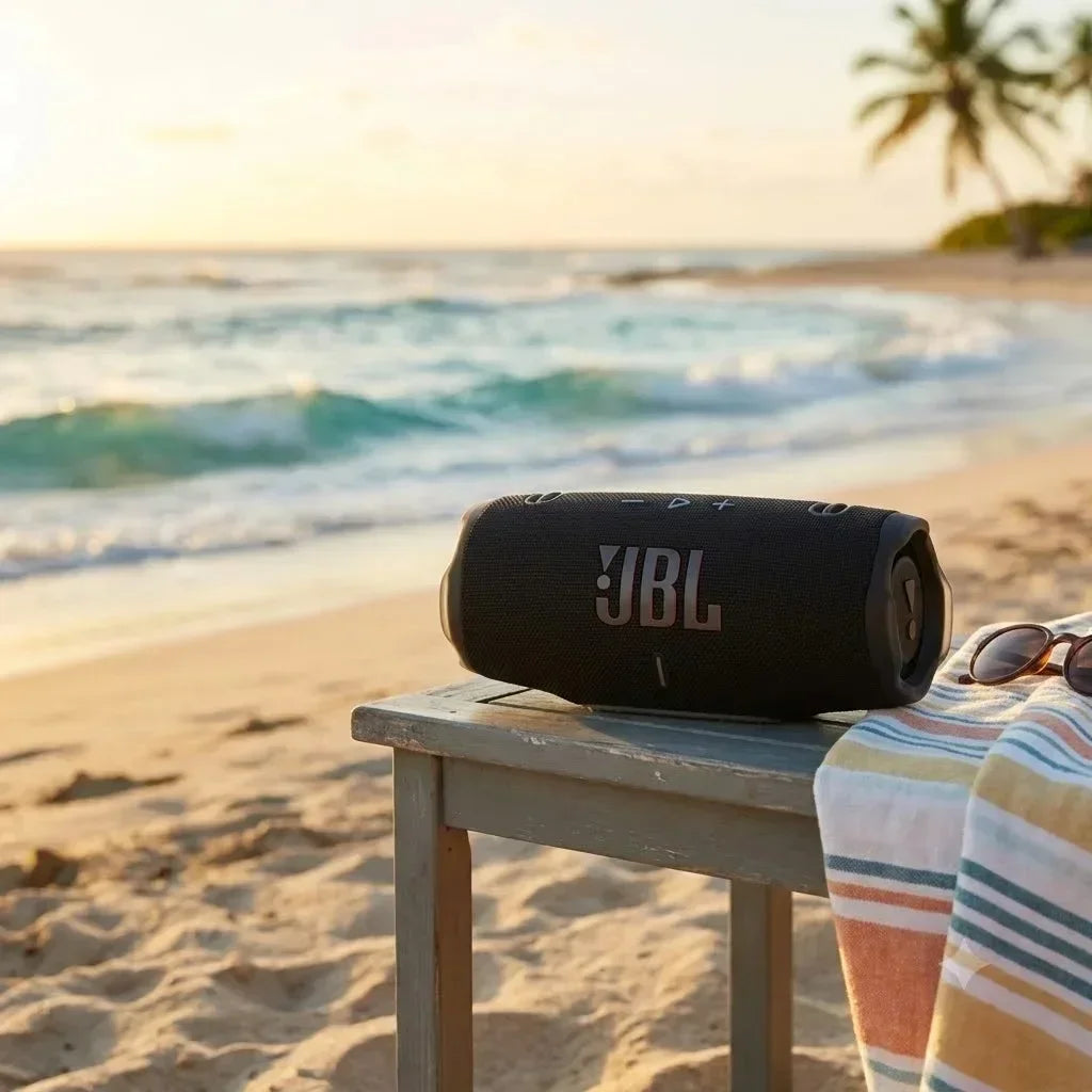 A black JBL Charge 6 portable speaker rests on a wooden surface near a beach at sunset.