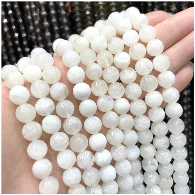 A hand holds multiple strands of round, translucent white natural stone beads for DIY jewelry making.