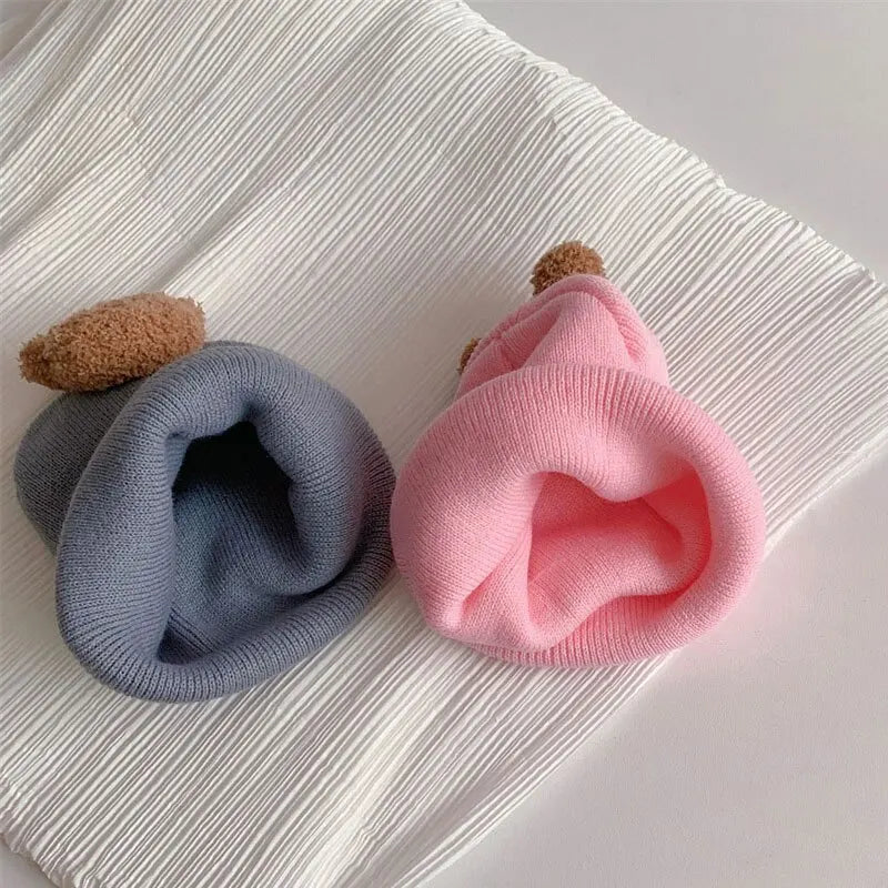A pink knitted baby hat with a brown pom-pom resting on a white ribbed fabric.
