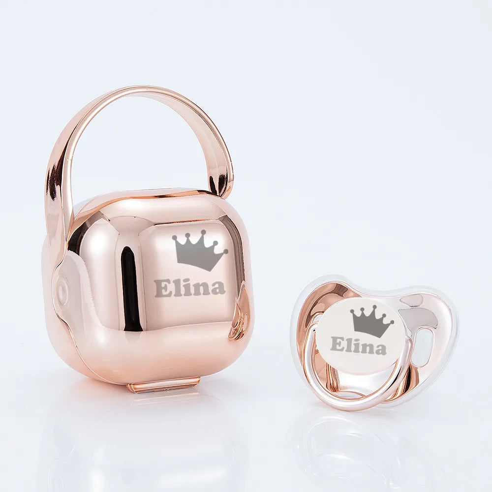 A rose gold personalized baby pacifier with a crown design and storage case.