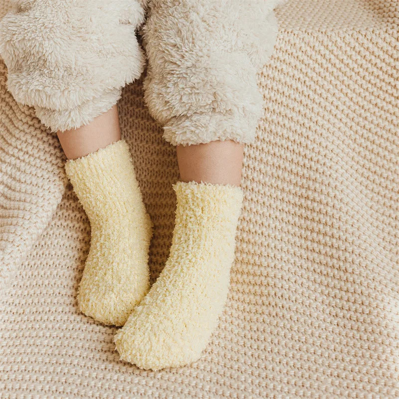 A pair of yellow knitted fleece socks worn by a person, resting on a beige knitted fabric.