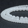 A string of small, round, natural white crystal quartz beads laid out on a dark surface.