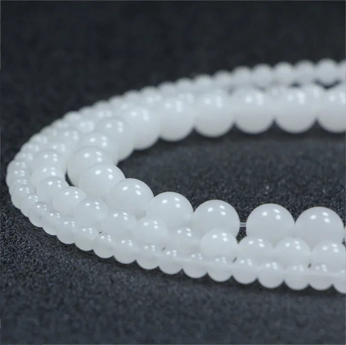A string of small, round, natural white crystal quartz beads laid out on a dark surface.