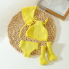 A yellow knitted doll outfit set featuring a hat, top, and three pairs of knitted socks on a woven mat.