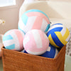 A basket filled with colorful soft plush volleyball pillows in pink, blue, and white.