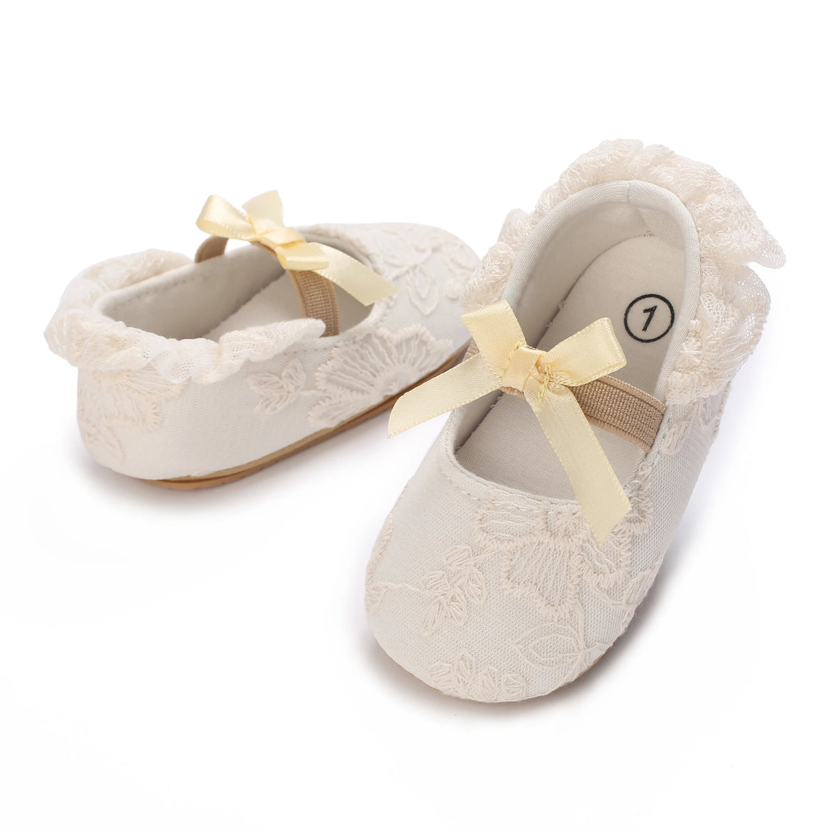 A pair of light beige lace-trimmed baby girl moccasin shoes with a yellow bow.