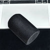 A black flocked foam microphone windscreen cover lying on a dark surface next to a laptop.