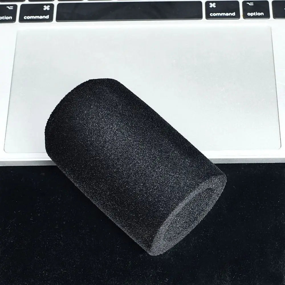 A black flocked foam microphone windscreen cover lying on a dark surface next to a laptop.
